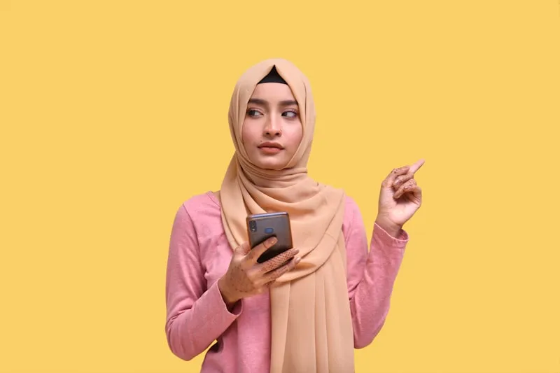 Woman in hijab holding phone and comparing AI headshot tools